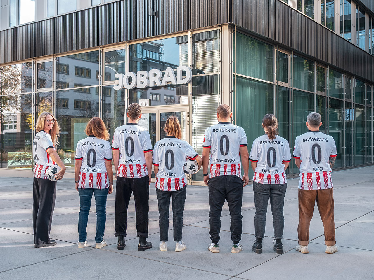 Mitarbeitende von JobRad stehen aufgereiht mit SC Trikots auf dem Campus, sie stehen mit dem Rücken zu uns und bilden 2000000 mit ihrer Trikotrückseite.